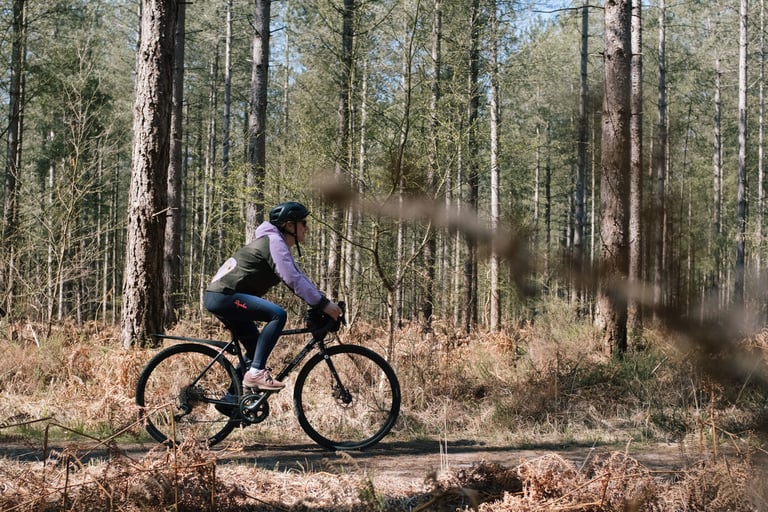 Rider in Rapha All Day Leggings on a gravel bike on a sandy track through pine woodland in the New Forest.