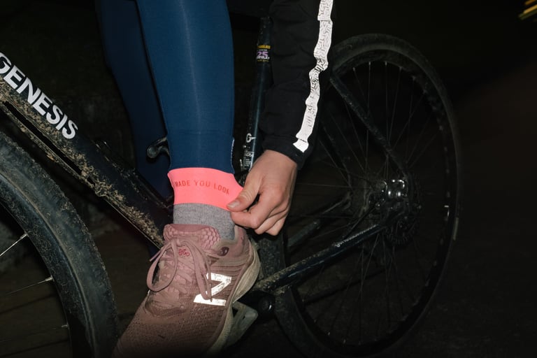 Hand turns up the cuff of Rapha All Day Leggings to show the pink 'made you look' panel, beside a Genesis bike.