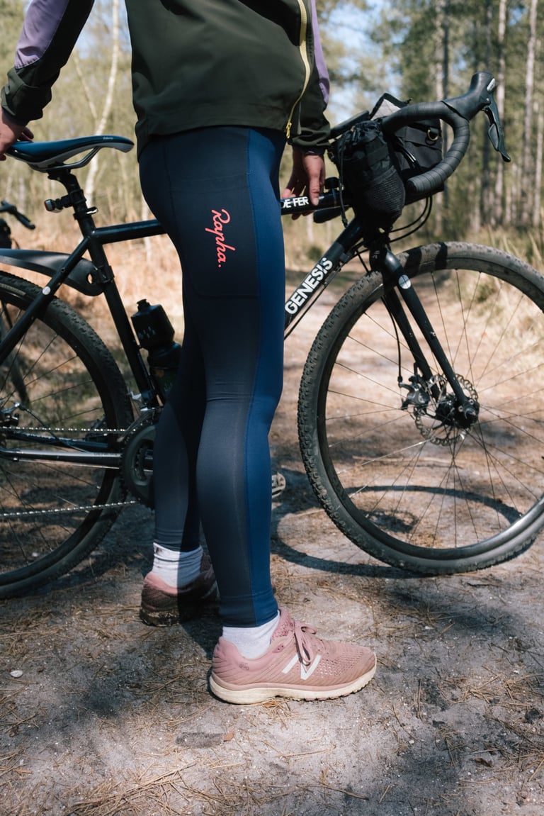 Full-length view of navy Rapha All Day Leggings with a thigh pocket, worn beside a Genesis gravel bike.
