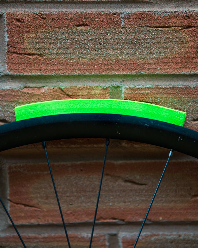 Arc of green Vittoria Air-Liner Gravel foam on a bare rim against a brick wall, showing its low profile.