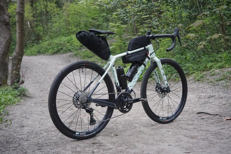 Pale green Canyon Grizl fitted with the Apidura collaboration frame bag and saddle pack on a woodland path.
