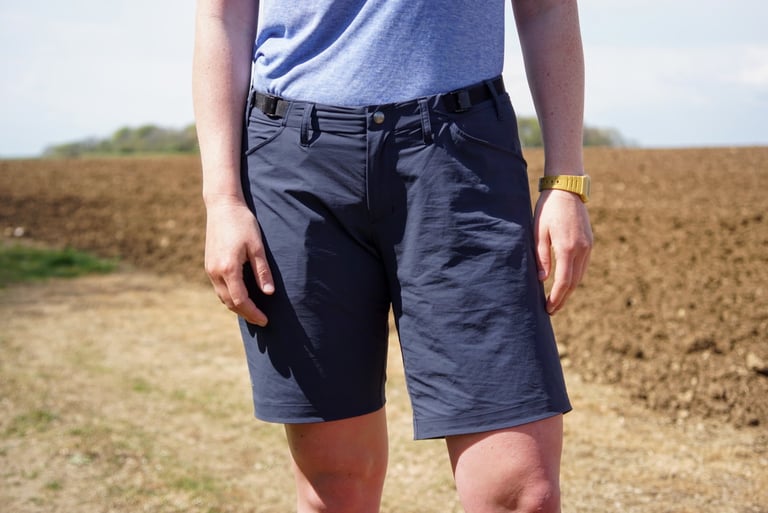 7mesh Farside short in navy, front view, with belt-style waist buckles and hand pockets, worn in a field.