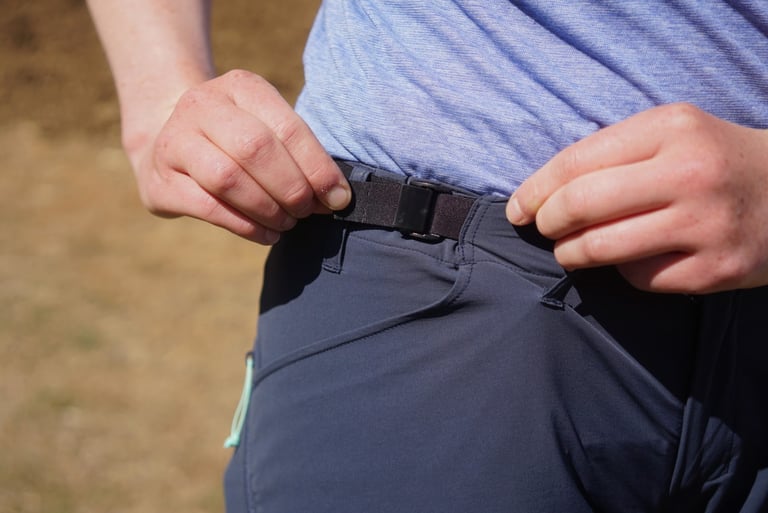 Hands adjusting the black webbing waistband buckle on the 7mesh Farside short.