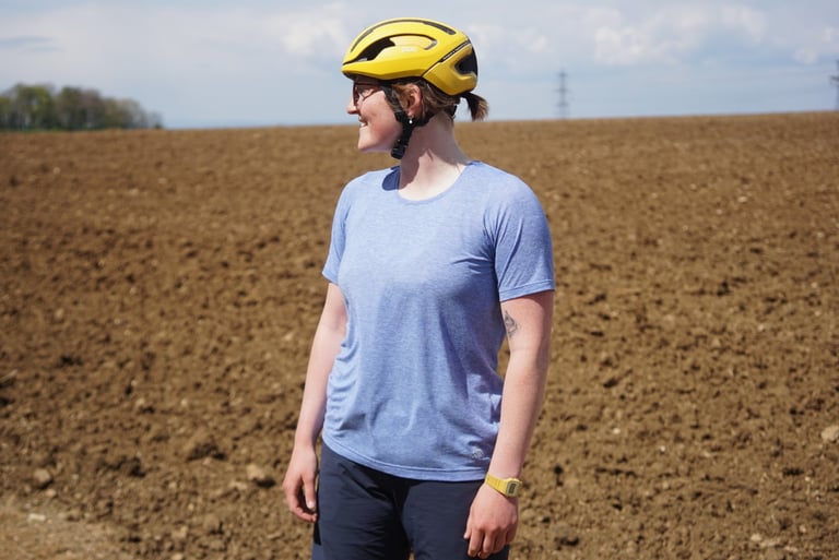 Rider in a pale blue 7mesh Elevate short sleeve tee and yellow helmet looks over a ploughed field.