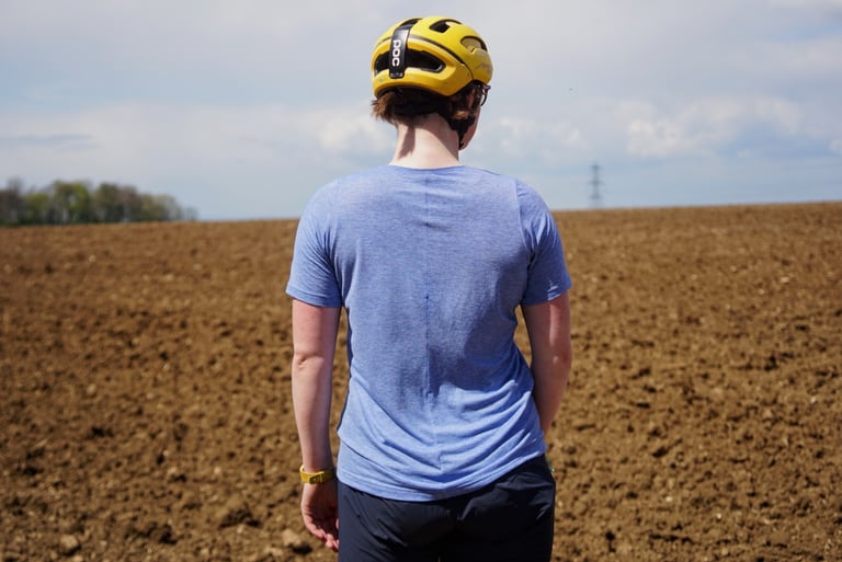 Back of the 7mesh Elevate tee showing the central back seam, worn with a yellow helmet by a field.