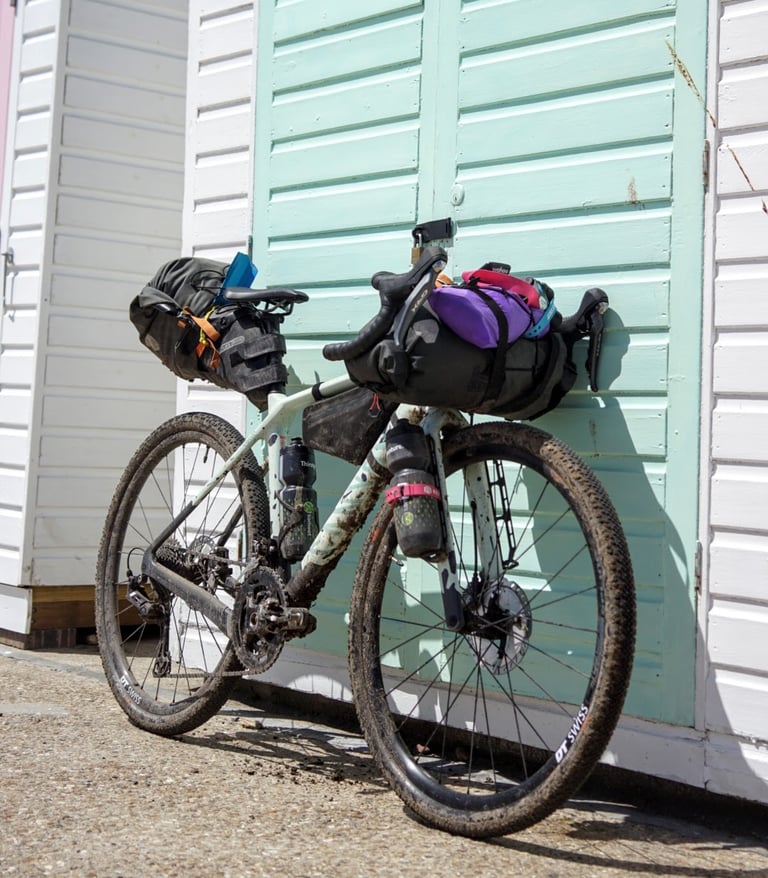 Loaded Canyon Grizl bikepacking setup leaning against a mint green beach hut door on the sea front.