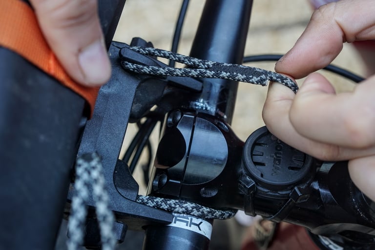 Fingers thread a grey dyneema cord around the stem to fit the Ortlieb Handlebar Pack QR mounting plate.