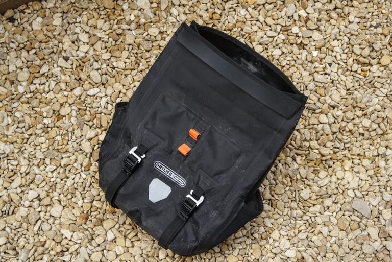 Ortlieb Handlebar Pack QR laid on gravel with its roll top open, showing buckles and logo.