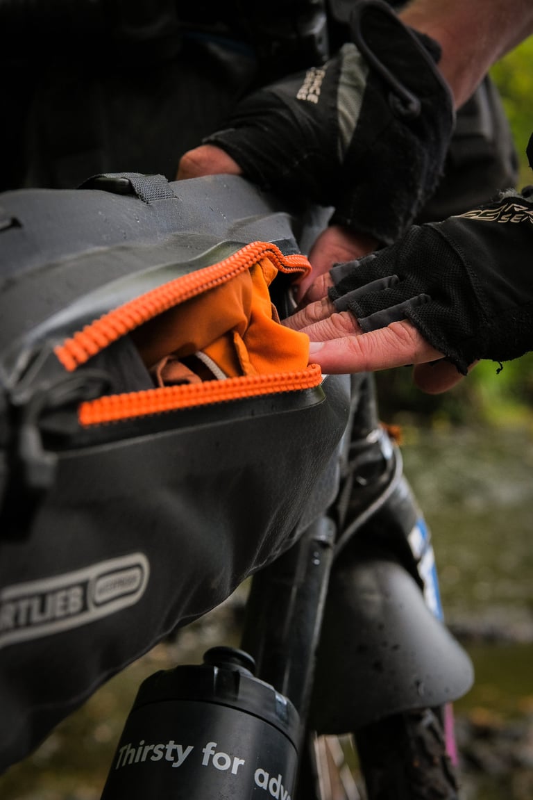 Gloved hand holds open the orange zip of an Ortlieb Frame-Pack to show an orange layer stowed inside.