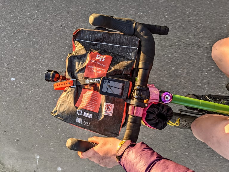 Bag of charcoal strapped to the front of a Fairlight Faran beside a Wahoo bike computer, seen from above.