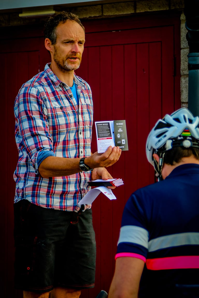 Focal Events' Andy holds up a briefing card to a helmeted rider at The Distance bikepacking event.