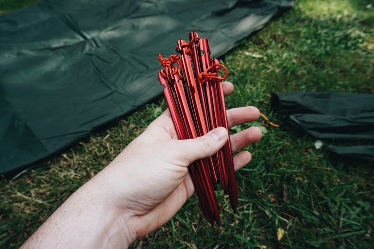 Hand holding a bunch of red anodised Y-beam aluminium pegs with paracord loops, supplied with the Alpkit Elan.