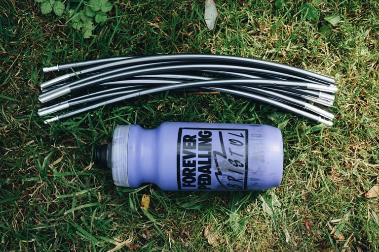 Folded aluminium poles from the Alpkit Elan hooped bivvy laid out on grass above a 500ml bottle for scale.