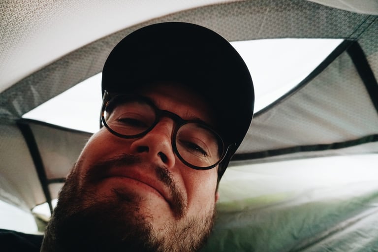 Person in glasses and a cap lying inside the Alpkit Elan hooped bivvy, looking up at the mesh above.