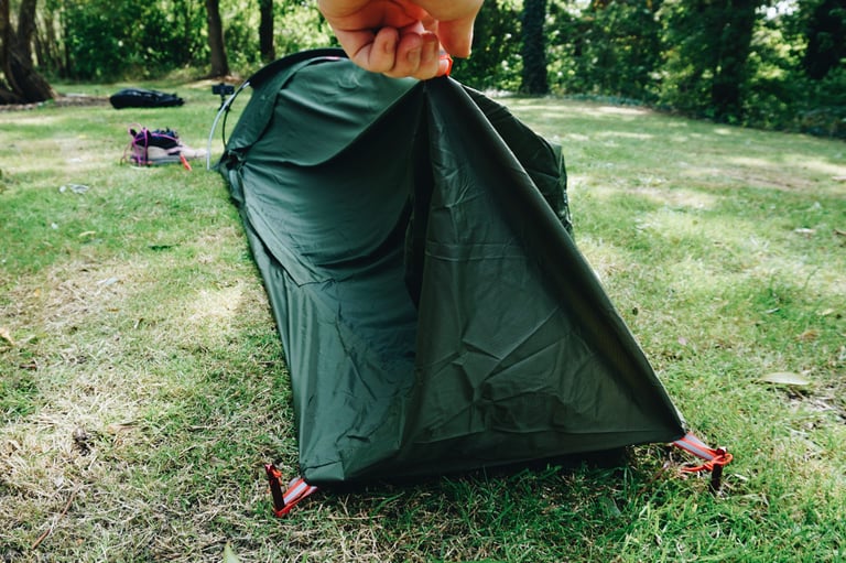 Pitched Alpkit Elan hooped bivvy with a hand lifting the foot-end flap, where a guy rope could be added.