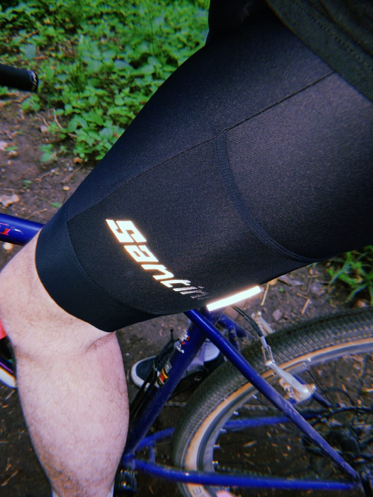 Reflective Santini logo on the thigh of the Gravel Bib shorts, with a reflective tab below, worn on a bike.