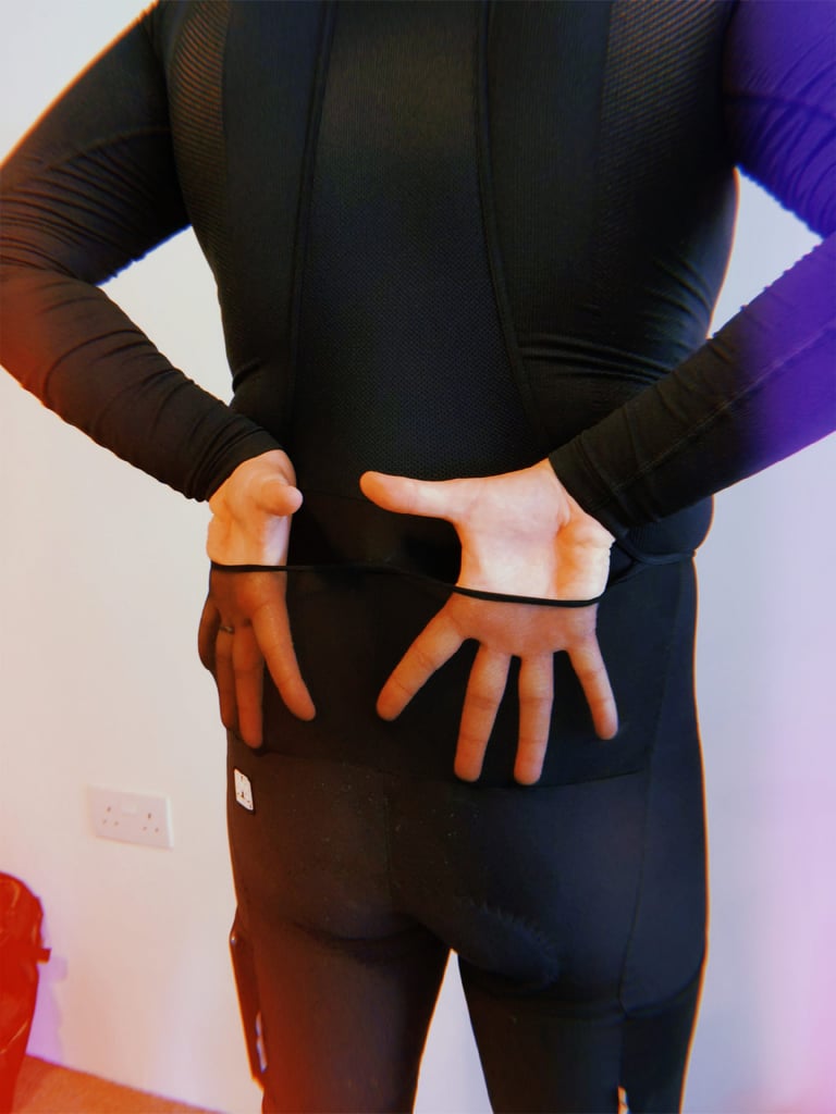 Rear view of the Santini Gravel Bib with both hands pulled behind the back, showing the split rear pocket.