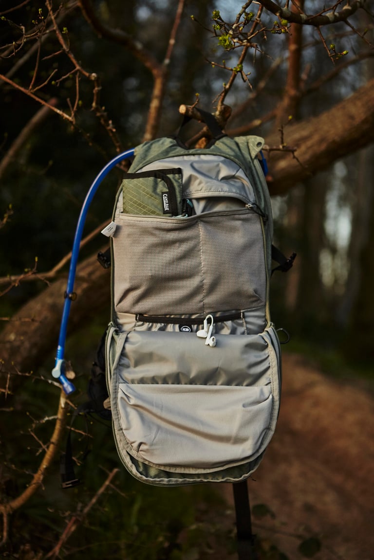 Camelbak Mule Pro hanging from a branch with its front panel open, showing mesh and zipped pockets.