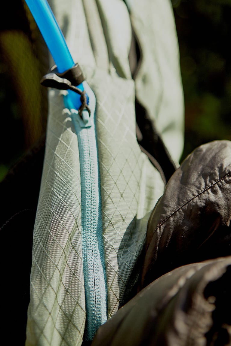 Camelbak Mule Pro hose clipped at the top of a pale blue side zip, with a black down jacket alongside.