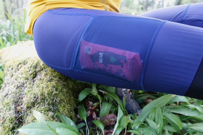 Snack packet in the stretch mesh thigh pocket of the Victory Chimp Out There bib shorts, rider seated on a mossy log.