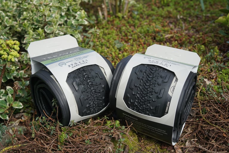 Two Teravail Sparwood 650b x 2.1 Hard Pack tyres still in their retail packaging, resting on moss and shrubs outdoors.