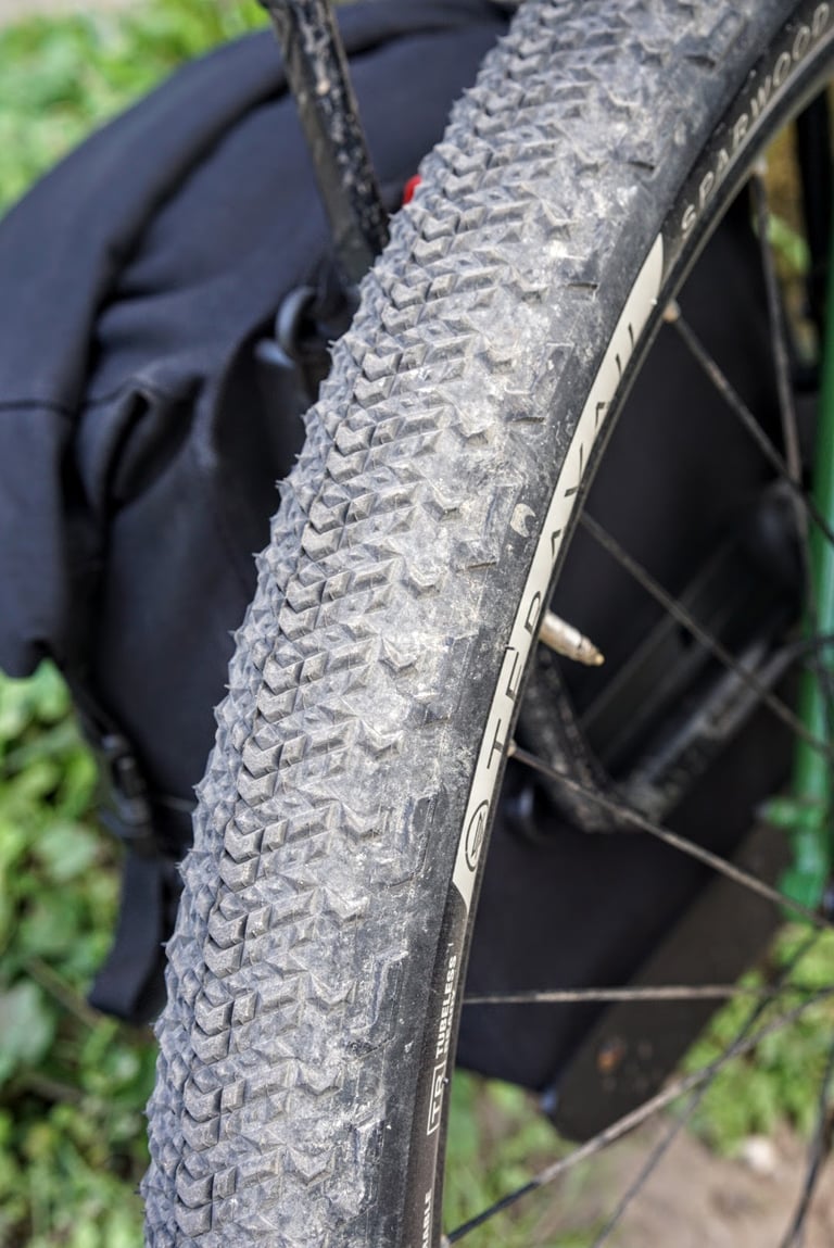 Teravail Sparwood 650b tyre, dusty from hardpack, on a loaded touring bike with a black pannier beside the front wheel.