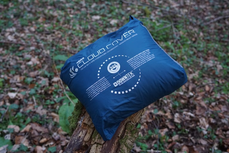 Alpkit Cloud Cover quilt packed into its own zipped pocket, a compact blue pack on a mossy log.