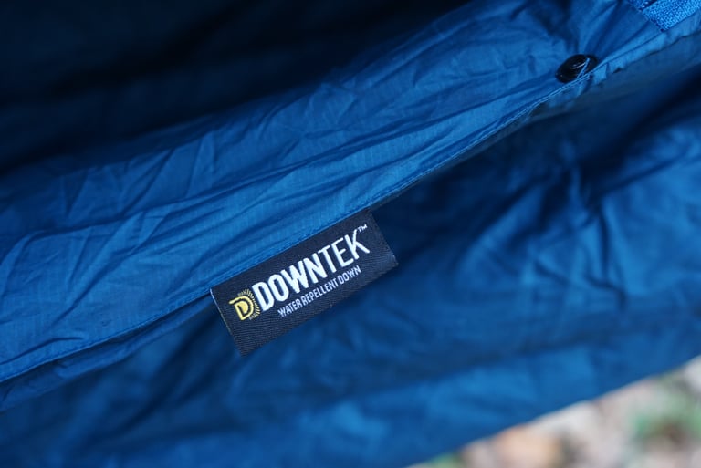 Downtek water repellent down label stitched on the blue Alpkit Cloud Cover quilt, next to a popper.