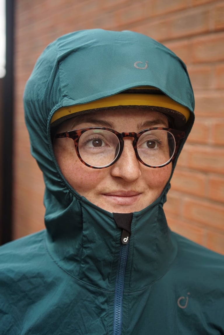 Rider wearing the Velocio jacket hood over a yellow helmet, showing the stiffened peak and zip garage.