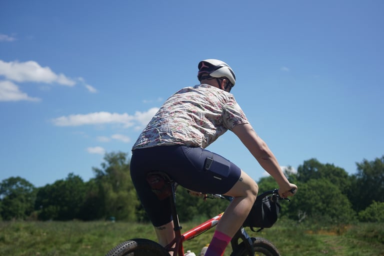 Rider on a red flat-bar bike with a handlebar bag crossing a sunny grass field in navy Triban RC500 bib shorts.
