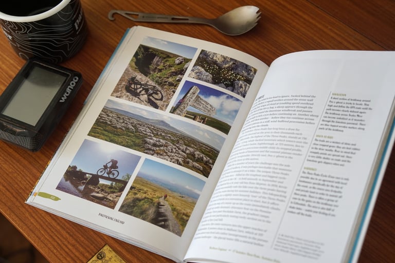Bikepacking England guidebook open on a route spread of photographs and notes, beside a Wahoo computer.