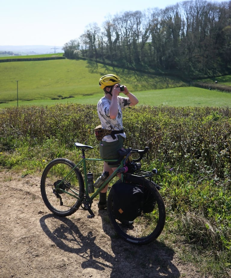 Rider in the Dioscvri Mystic Felines tee photographs the view beside a green touring bike with panniers.