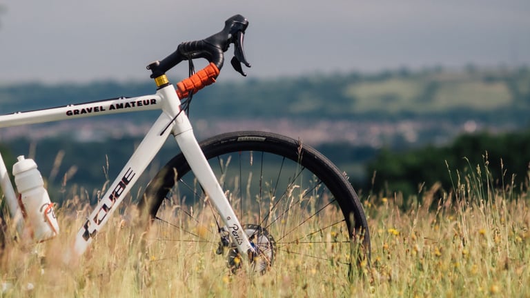 Teravail Rampart tyre on a white Cube cross bike standing in long summer grass, with hills in the distance.