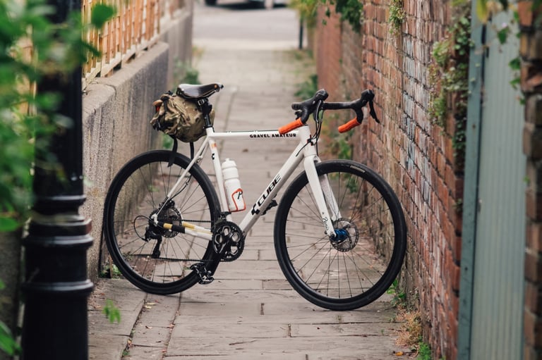 White Cube cross bike with a saddle bag propped in a narrow brick-walled alley, fitted with Teravail Rampart tyres.