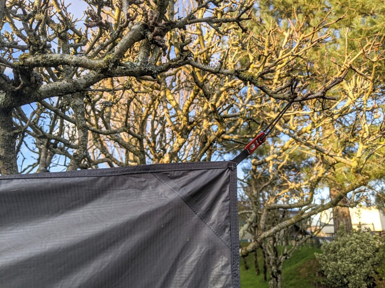 Grey Jaran 2 tent panel hung from a tree branch by a red tensioner, drying in the sun.