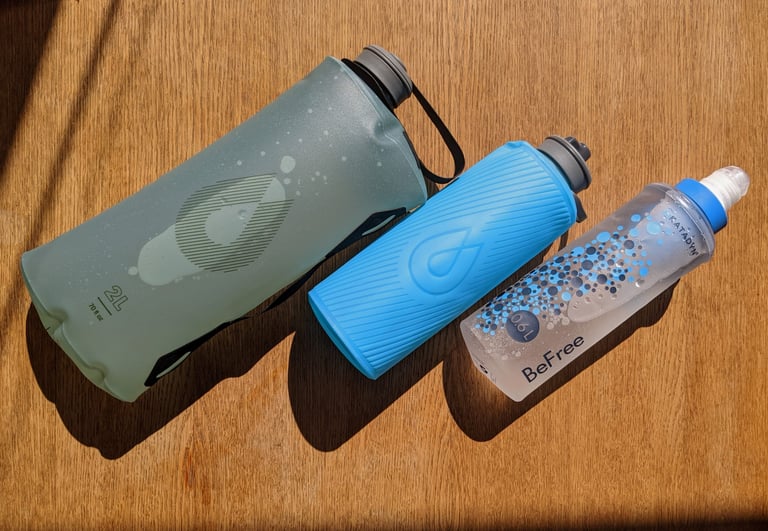 HydraPak Seeker 2L, Flux 1L and Katadyn BeFree 0.6L soft flasks laid side by side on a wooden table.