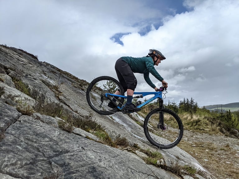 Rider in the Velocio Ultralight Hooded Jacket descends a steep rock slab on a blue Santa Cruz mountain bike.