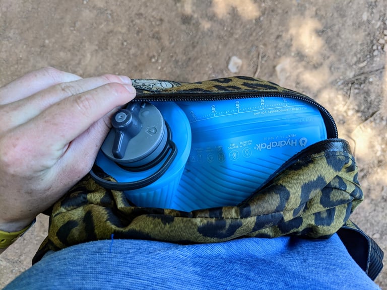 HydraPak Flux 1L soft bottle tucked into an open leopard-print hip pack for a hot-weather ride.