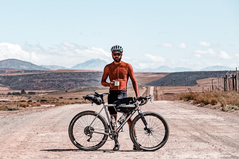 Rae Trew-Browne with a bikepacking gravel bike on a dusty road in South Africa, holding a mug.