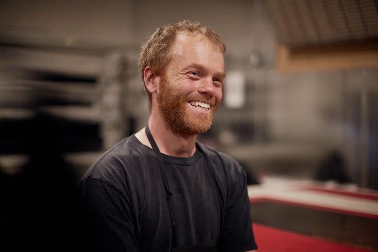Carl from Restrap grins in a black T-shirt and apron on the workshop floor before heading off to race the TransEngland.