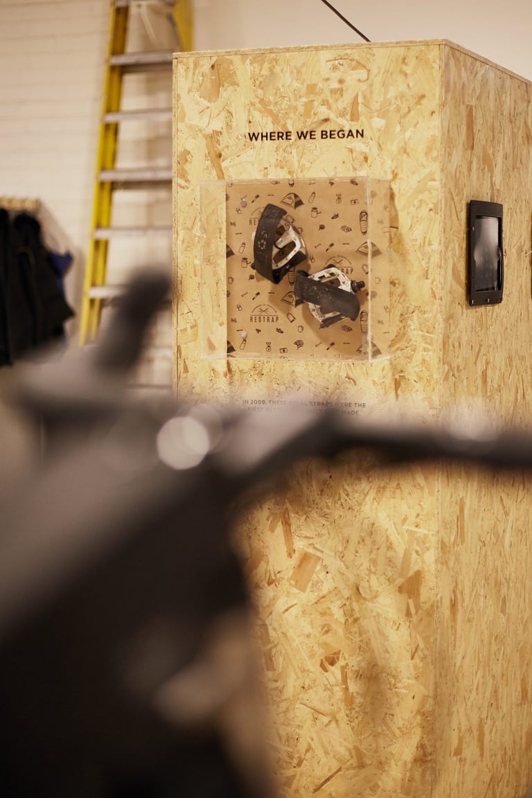 Restrap's first pedal straps in a display case marked 'Where we began' on a chipboard plinth in the Leeds workshop.