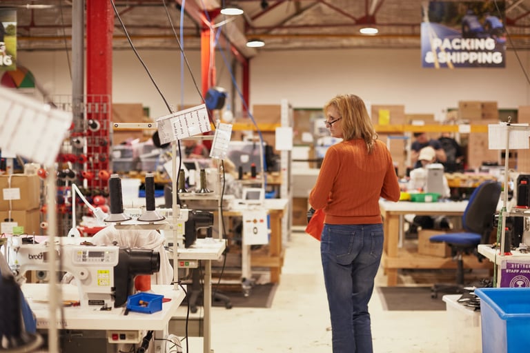 Worker in an orange jumper walks between rows of industrial sewing machines on the Restrap workshop floor in Leeds.