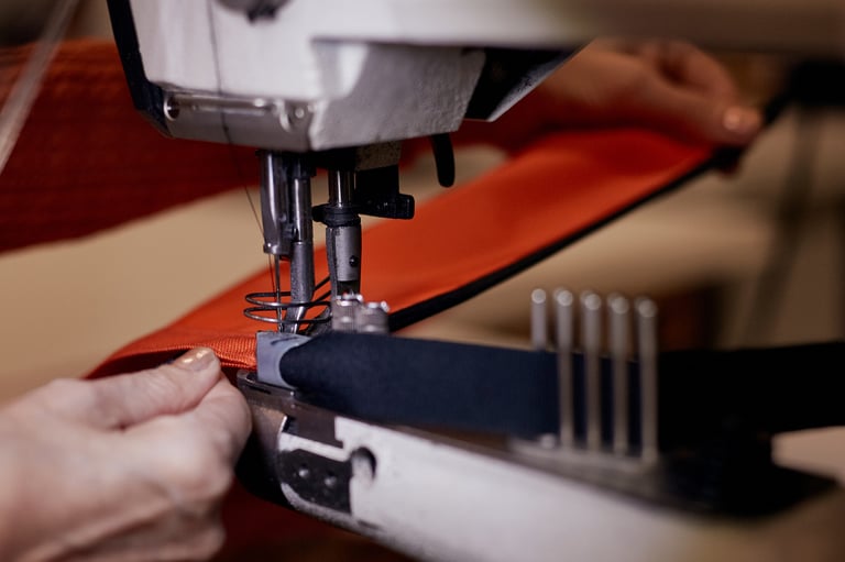 Machinist guides orange fabric under the needle of an industrial sewing machine at Restrap's Leeds workshop.