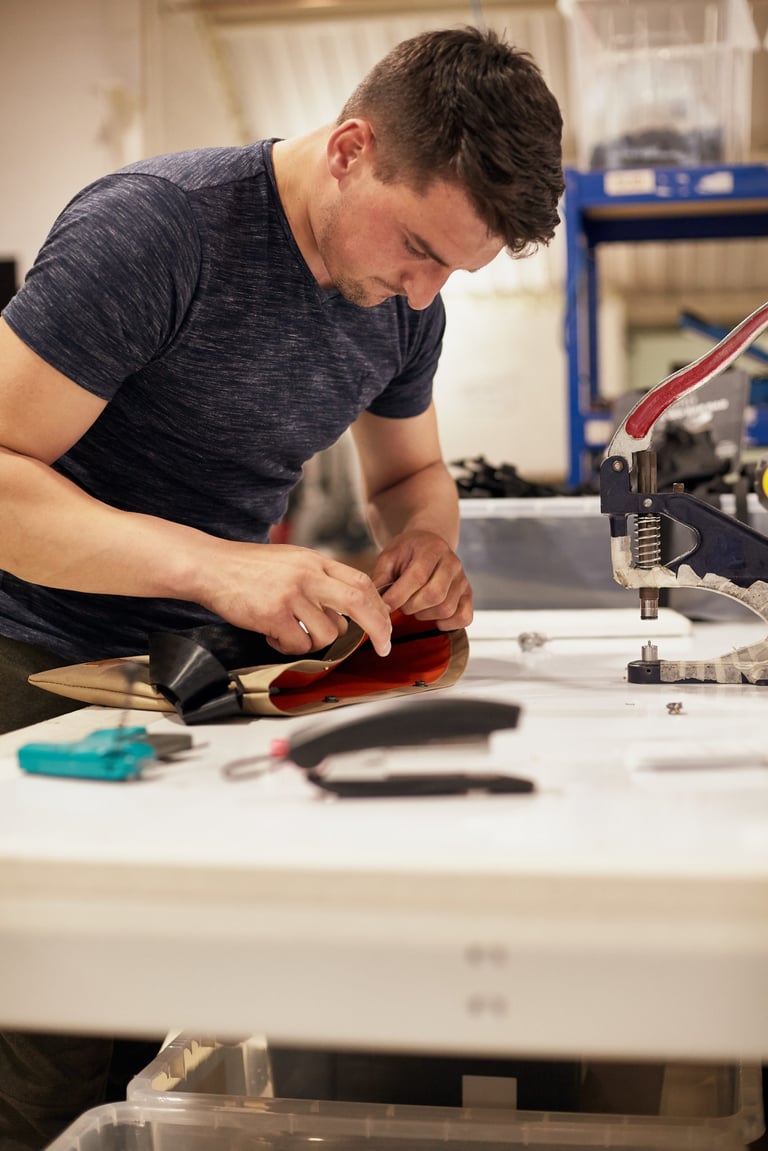 Marius from the Restrap packing team fits poppers to a sandy and orange musette beside a hand press.