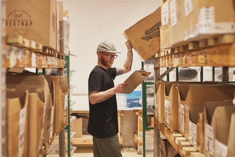 Restrap staff member checks a clipboard between shelves of boxed stock in the Leeds workshop.