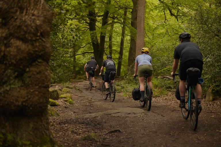 Rider in Machines For Freedom Key Shorts climbs a rocky woodland trail with three other riders on gravel bikes.