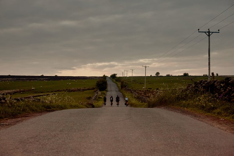 Four riders on loaded bikes head along a quiet road beneath a grey evening sky above Askwith.