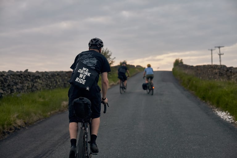 Rider with a musette slung across their back climbs a stone-walled lane towards Weston Moor Road at dusk.