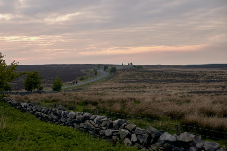 Riders on a winding road across open moorland at sunset on Weston Moor Road in the Yorkshire Dales.