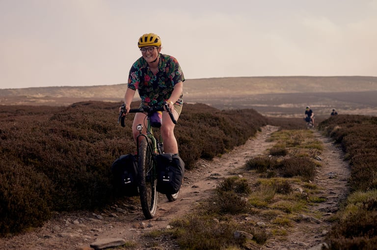 Smiling rider with Restrap front panniers rides a stony track through open heather moorland.